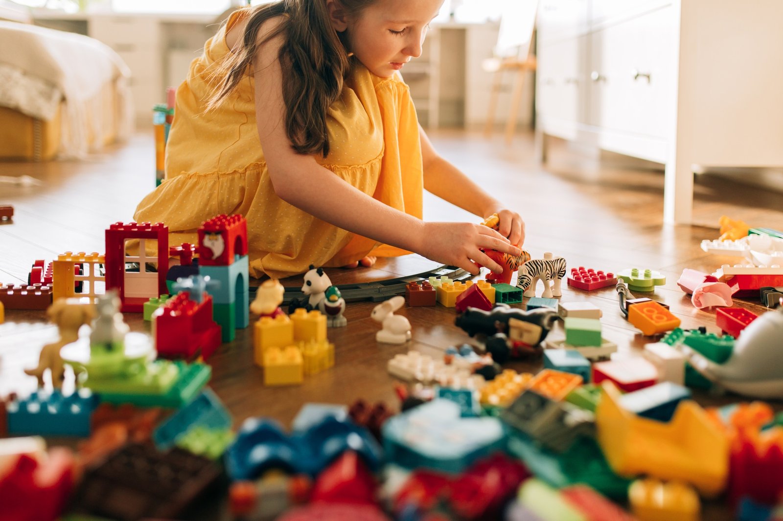 Little toddler girl playing with colourful Lego blocks at home alone