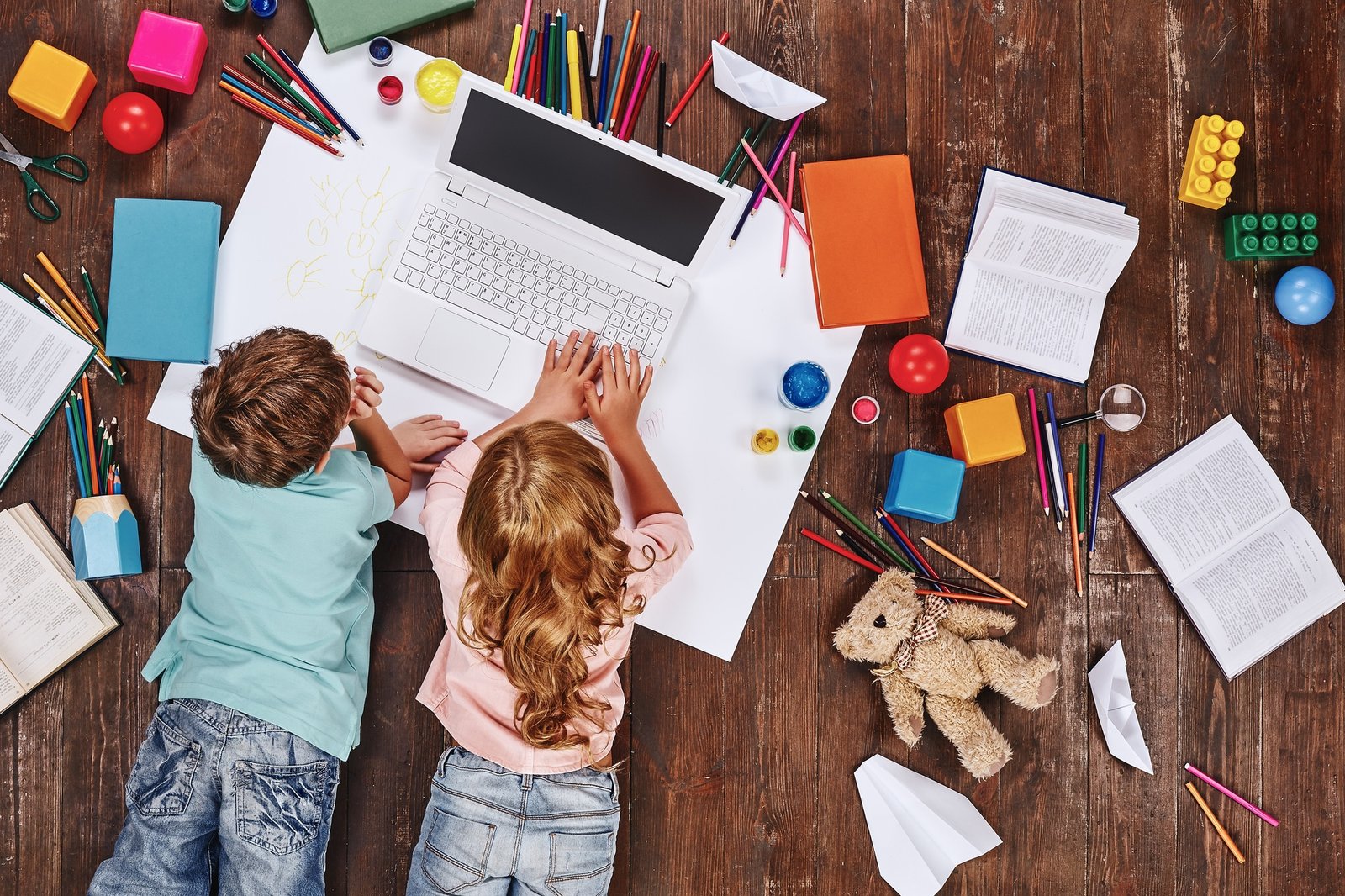 There are so many things. Children lying near books and toys, while playing on toy computer